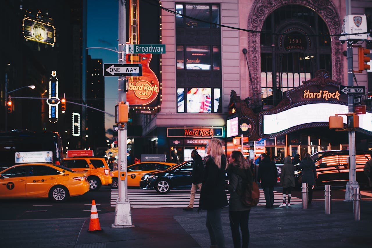 services-02 A bustling street view of Broadway at night featuring Hard Rock Cafe, taxis, and pedestrians in New York City.