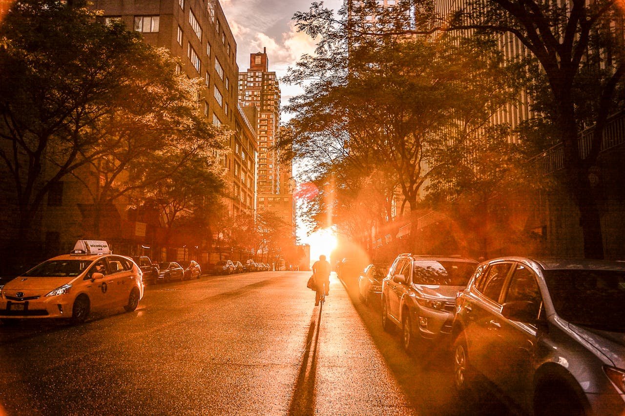 services-03 Silhouette of a cyclist during sunset on a New York City street with urban buildings and cars.